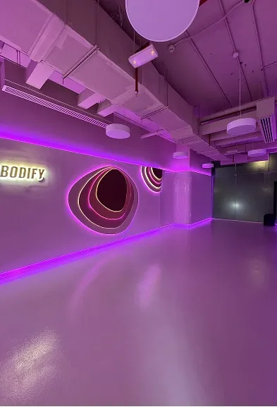 Spacious workout room with neon wall lighting and BODIFY branding in the club interior