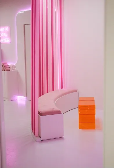 Curved bench with pink dividers and an orange acrylic side table in the lounge area of the fitness studio
