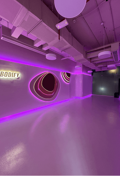 Spacious workout room with neon wall lighting and BODIFY branding in the club interior
