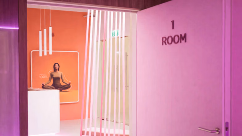 Minimalist pink fitness studio room with a woman meditating inside a glass training space