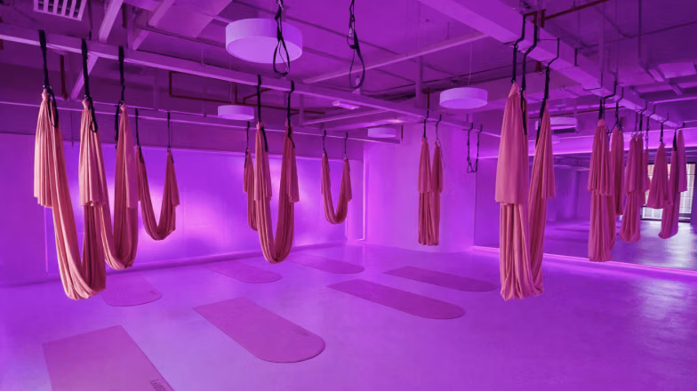 Spacious gym studio with aerial hammocks for anti-gravity yoga under purple lighting