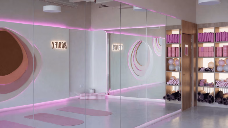 Bright modern fitness studio interior with mirrors and soft pink lighting design