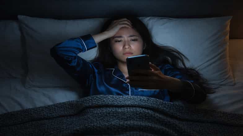 Woman lying in bed at night and looking at her phone with a worried expression