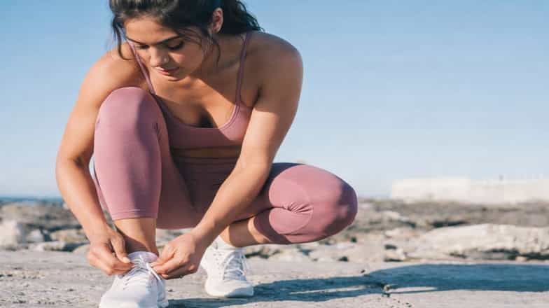 Woman in pink activewear tying her sneaker outdoors before a workout