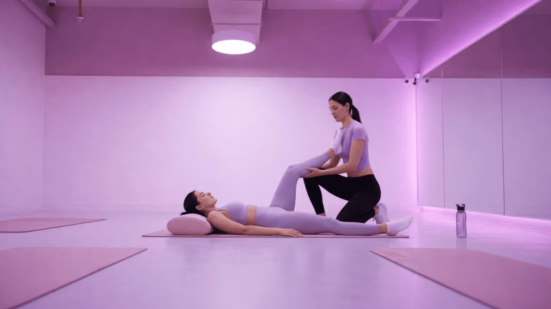 Trainer helping a client with assisted stretching in a studio, improving flexibility and range of motion