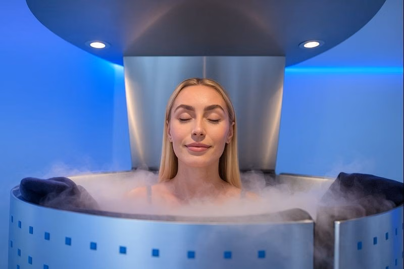 Woman undergoing cryotherapy session with cold mist surrounding her in a recovery chamber